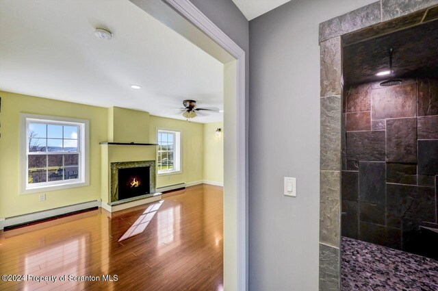 living room featuring ceiling fan, baseboard heating, and a wealth of natural light