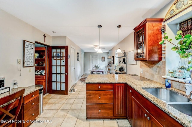 kitchen featuring kitchen peninsula, light stone countertops, backsplash, sink, and pendant lighting