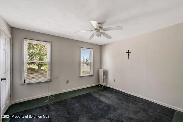 empty room featuring ceiling fan, radiator heating unit, and dark carpet