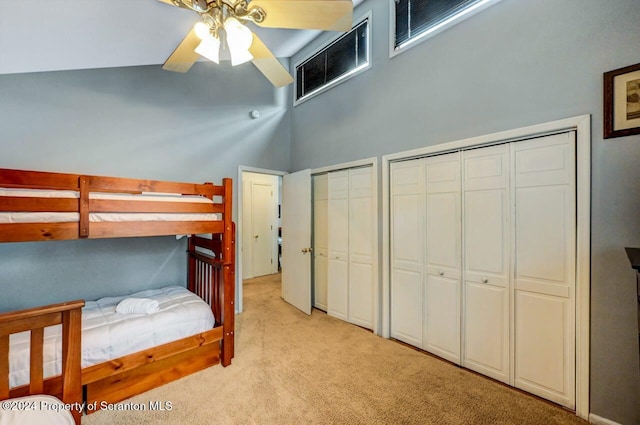 bedroom with ceiling fan, high vaulted ceiling, light carpet, and two closets