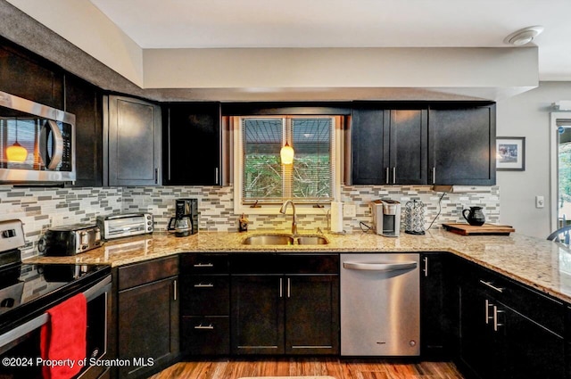 kitchen with sink, light hardwood / wood-style flooring, decorative backsplash, appliances with stainless steel finishes, and light stone counters