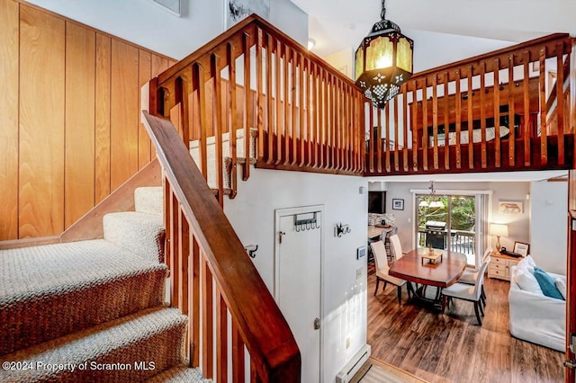 staircase featuring baseboard heating, high vaulted ceiling, and wood-type flooring