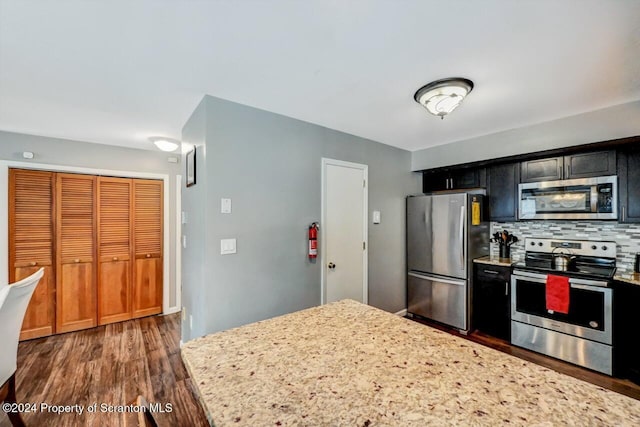 kitchen featuring light stone countertops, appliances with stainless steel finishes, tasteful backsplash, and dark wood-type flooring