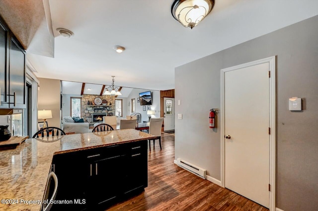 kitchen with a stone fireplace, light stone counters, baseboard heating, dark hardwood / wood-style flooring, and a chandelier