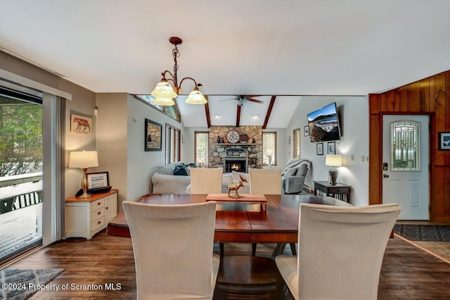 dining space featuring vaulted ceiling with beams, a healthy amount of sunlight, a stone fireplace, and ceiling fan with notable chandelier