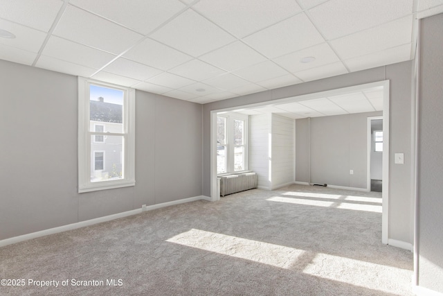 spare room with radiator heating unit, light colored carpet, plenty of natural light, and a drop ceiling