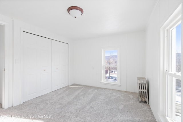 unfurnished bedroom featuring light colored carpet, multiple windows, radiator, and a closet