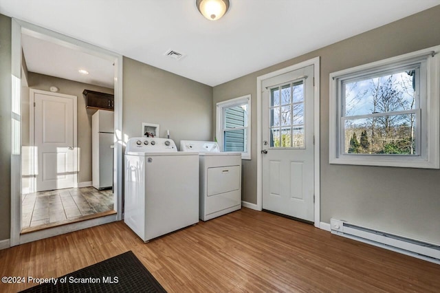 clothes washing area with washer and dryer, light hardwood / wood-style floors, and a baseboard heating unit