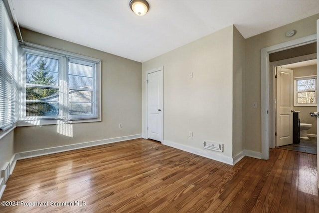 unfurnished bedroom with ensuite bath and hardwood / wood-style floors