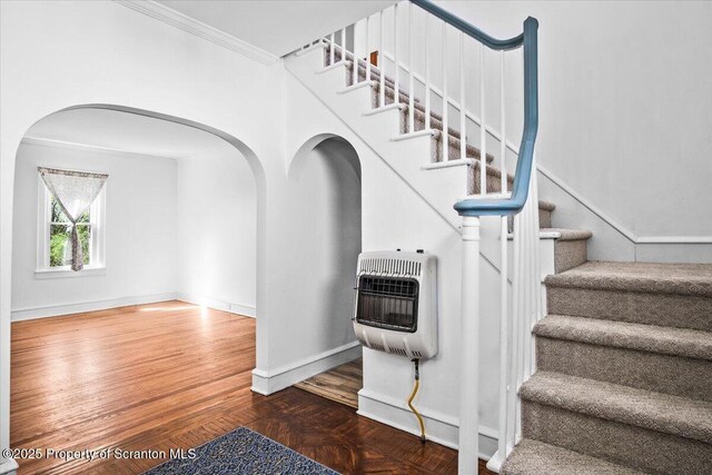 stairs featuring arched walkways, parquet floors, baseboards, heating unit, and ornamental molding