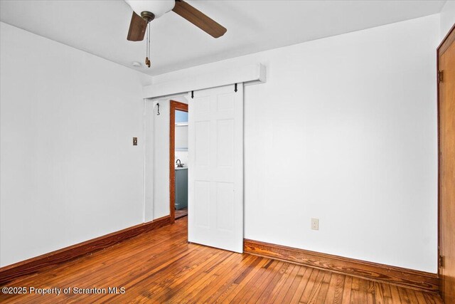 unfurnished room with ceiling fan, a barn door, baseboards, and hardwood / wood-style flooring