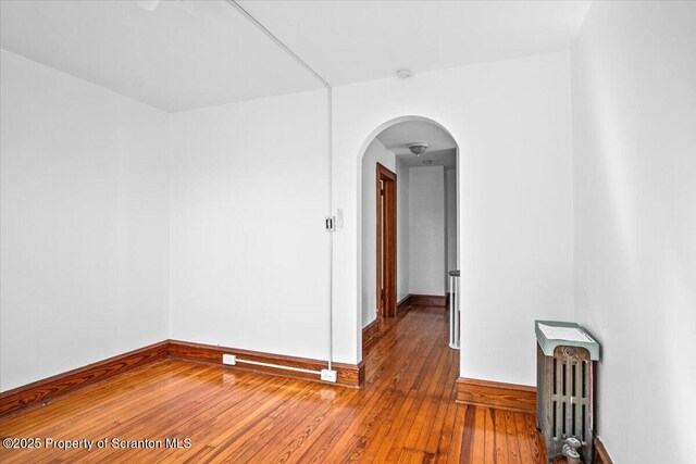 unfurnished room with wood-type flooring, arched walkways, baseboards, and radiator heating unit