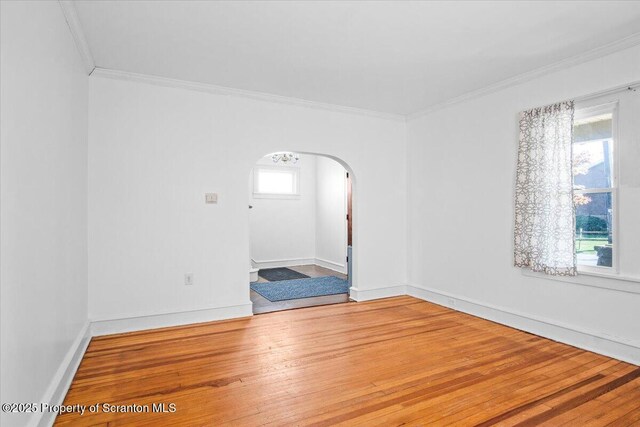 unfurnished room with crown molding, arched walkways, baseboards, and wood finished floors
