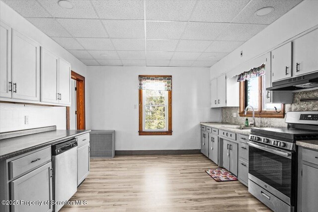 kitchen featuring a drop ceiling, under cabinet range hood, a sink, backsplash, and stainless steel appliances