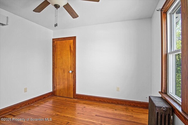 spare room featuring baseboards, a ceiling fan, radiator, and hardwood / wood-style flooring