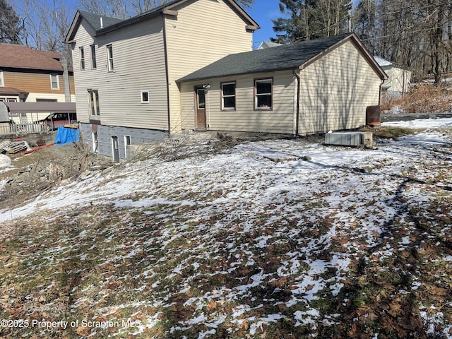 snow covered rear of property featuring central AC