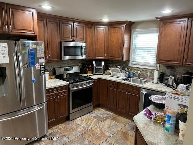 kitchen featuring stainless steel appliances, light countertops, a sink, and decorative backsplash