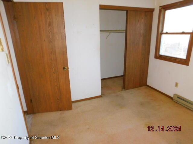 unfurnished bedroom featuring light colored carpet, baseboard heating, and a closet