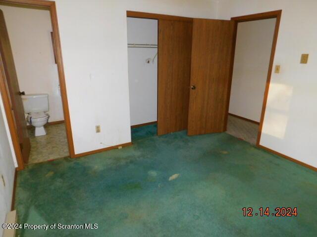 unfurnished bedroom featuring dark colored carpet, connected bathroom, and a closet