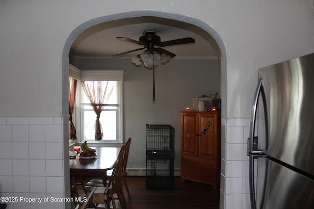 dining room with arched walkways, tile walls, ceiling fan, and ornamental molding