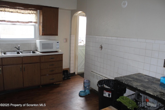 kitchen featuring a sink, radiator heating unit, arched walkways, tile walls, and white microwave