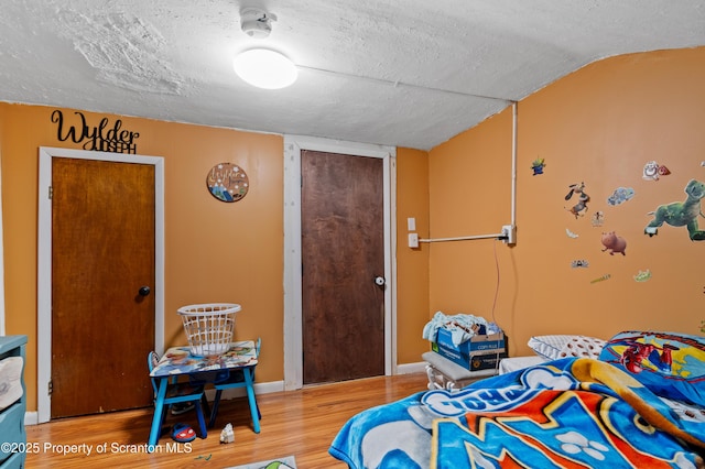 bedroom featuring hardwood / wood-style flooring, vaulted ceiling, and a textured ceiling