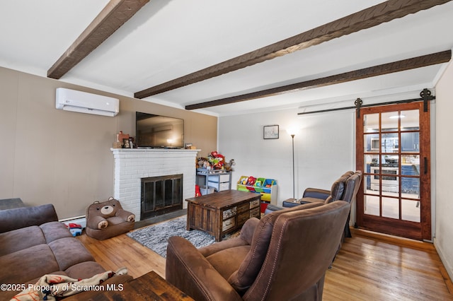 living room featuring an AC wall unit, light hardwood / wood-style floors, a barn door, beam ceiling, and a brick fireplace