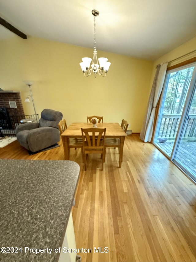 dining room with beamed ceiling, a notable chandelier, hardwood / wood-style floors, and a brick fireplace