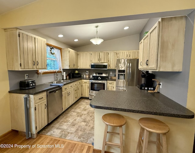 kitchen with light brown cabinetry, stainless steel appliances, vaulted ceiling, sink, and a breakfast bar area