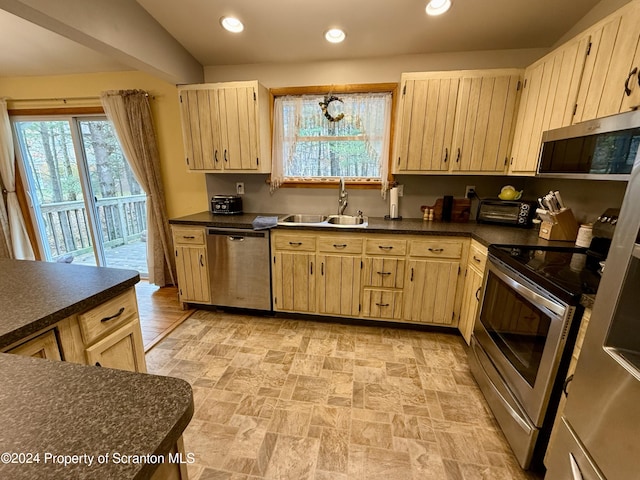 kitchen featuring appliances with stainless steel finishes, light brown cabinets, vaulted ceiling, and sink