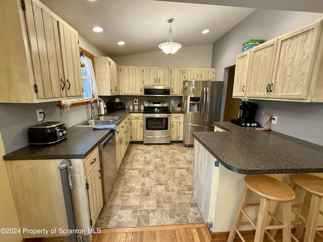 kitchen with stainless steel appliances, sink, light brown cabinets, decorative light fixtures, and a breakfast bar area