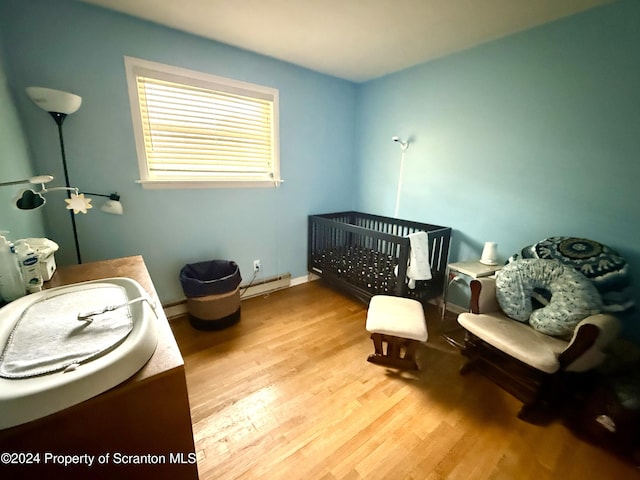 bedroom with light hardwood / wood-style flooring, a nursery area, and a baseboard heating unit