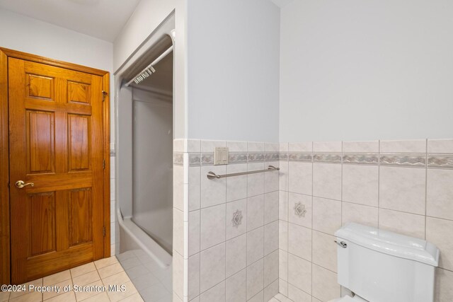 bathroom featuring tile patterned floors, toilet, tile walls, and enclosed tub / shower combo