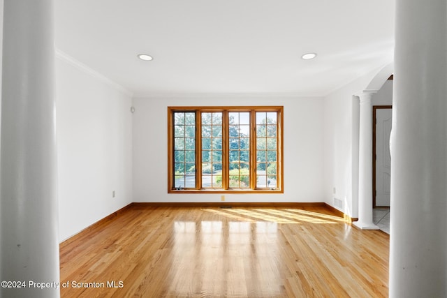 empty room featuring light hardwood / wood-style flooring, ornate columns, and crown molding