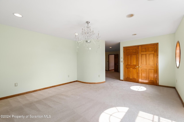 empty room with light colored carpet and a notable chandelier