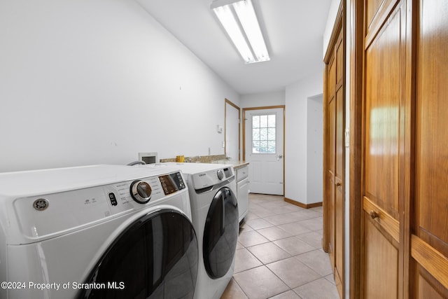 clothes washing area featuring washer and dryer, light tile patterned flooring, and cabinets