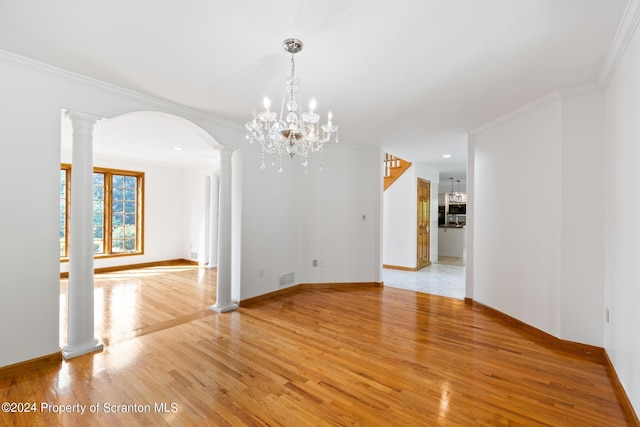 unfurnished room featuring ornate columns, ornamental molding, light wood-type flooring, and an inviting chandelier