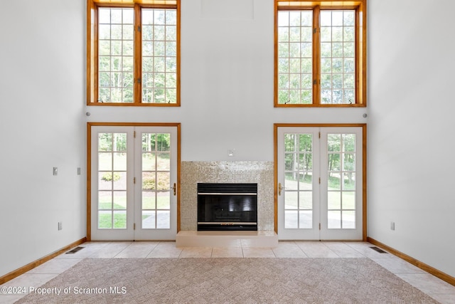 unfurnished living room with french doors, a towering ceiling, a healthy amount of sunlight, and light tile patterned flooring