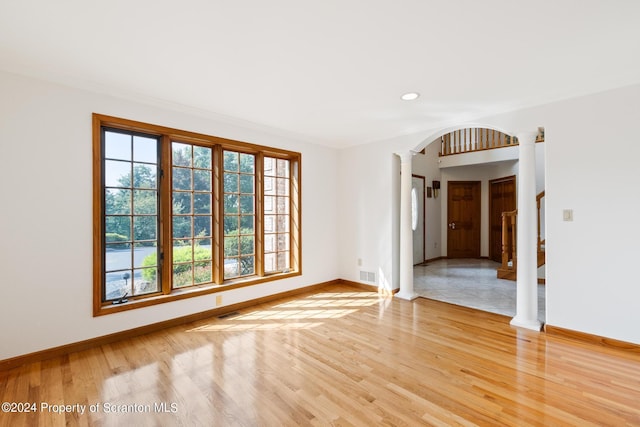 empty room featuring hardwood / wood-style floors, ornate columns, and ornamental molding