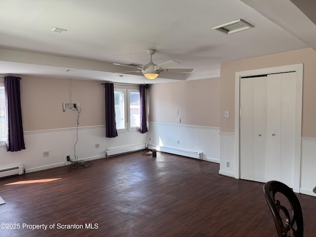 empty room with a ceiling fan, wood finished floors, visible vents, and a baseboard heating unit