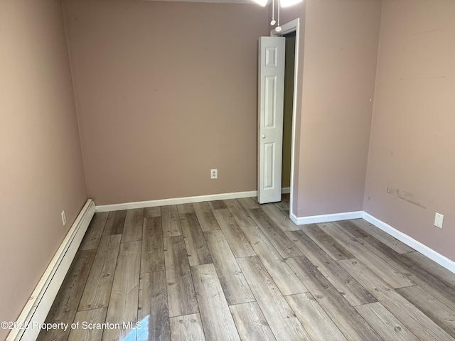 spare room featuring a baseboard heating unit, baseboards, and wood finished floors