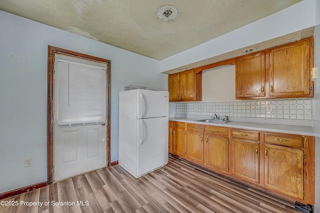 kitchen with brown cabinets, a sink, light countertops, freestanding refrigerator, and light wood finished floors