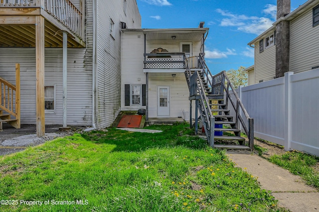 back of property featuring stairway, a lawn, and fence