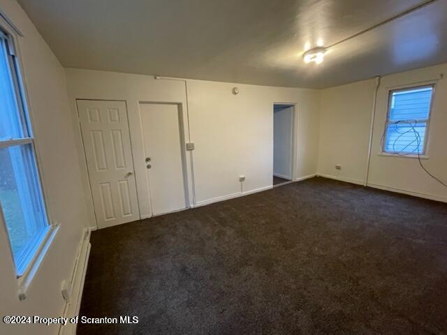 carpeted empty room featuring a baseboard heating unit