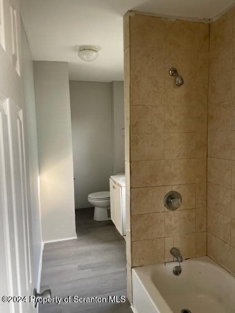 full bathroom with tiled shower / bath, hardwood / wood-style flooring, vanity, and toilet