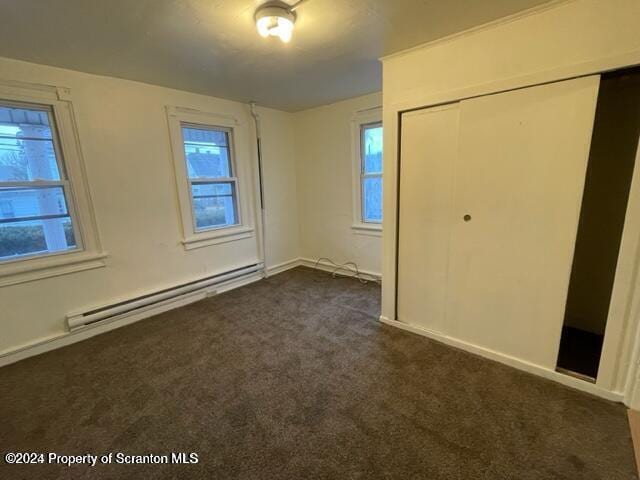 unfurnished bedroom featuring dark colored carpet, baseboard heating, and a closet