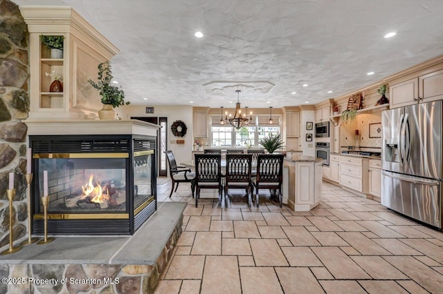 214 Oak St, Dunmore, PA 18512 - kitchen with stainless steel appliances, a multi sided fireplace, cream cabinetry, a chandelier, and a kitchen island