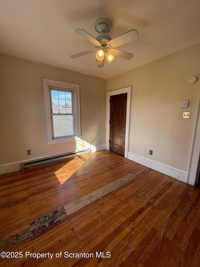 spare room featuring a baseboard heating unit, ceiling fan, wood-type flooring, and baseboards