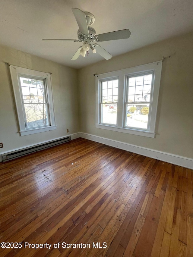 spare room with a baseboard heating unit, plenty of natural light, dark wood finished floors, and baseboards