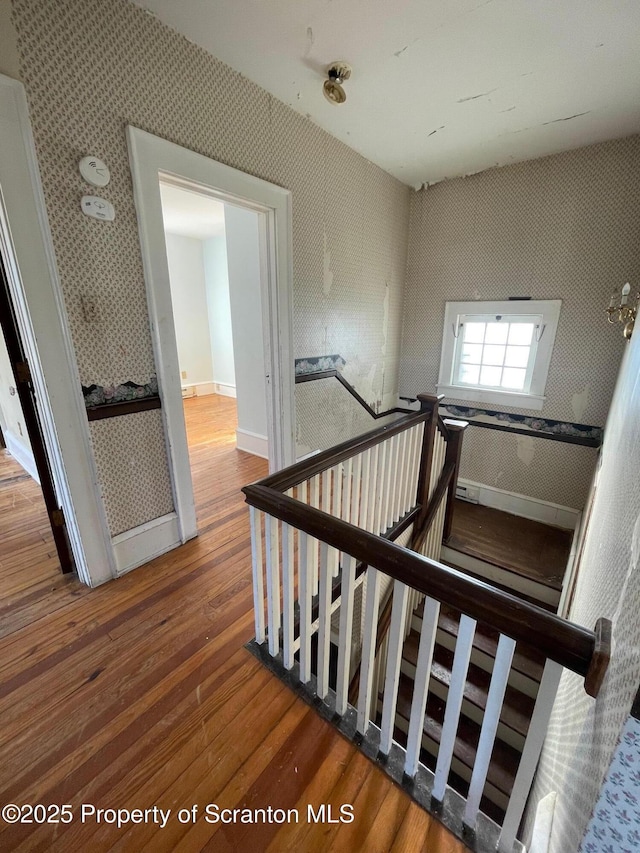 staircase with wood finished floors, baseboards, and wallpapered walls